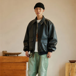 Person wearing a dark leather jacket and light green pants standing against a neutral background.