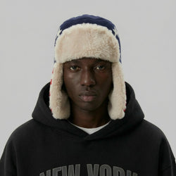 Person wearing a dark hoodie and a fur-trimmed hat on a plain background