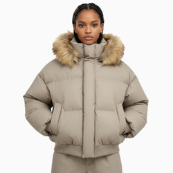 Person wearing a beige puffer jacket with fur hood on a white background