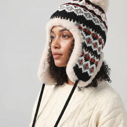 Person wearing a knitted hat with ear flaps and a floral pattern on a plain background